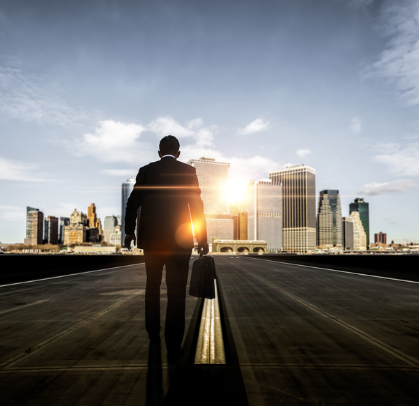 A man in a suit, carrying a briefcase, walking down a road towards a futuristic city skyline in the distance