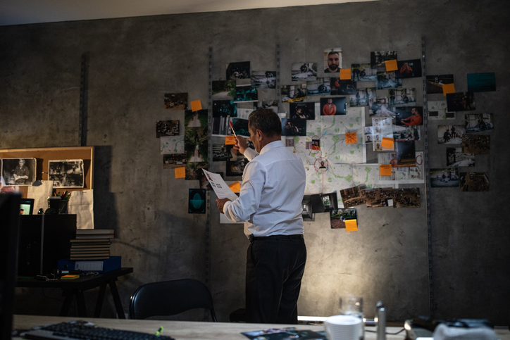 Detective looking at the paper in front of the wall with map and pictures at office