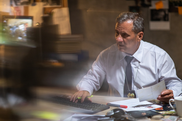 A government investigator with one hand on the keyboard and one hand on a document