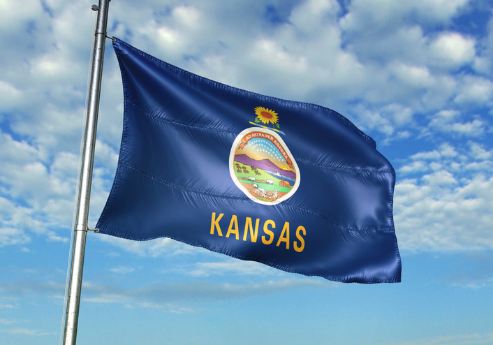 Kansas state flag flying on flagpole with a blue sky and clouds background