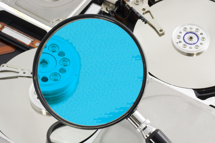 A magnifying glass over a opened hard drive depicting computer forensic