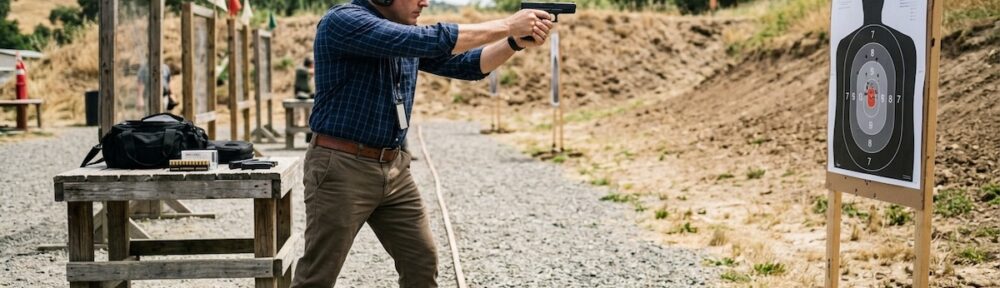 Private investigator completing firearms qualification at outdoor shooting range, proper stance, ear and eye protection